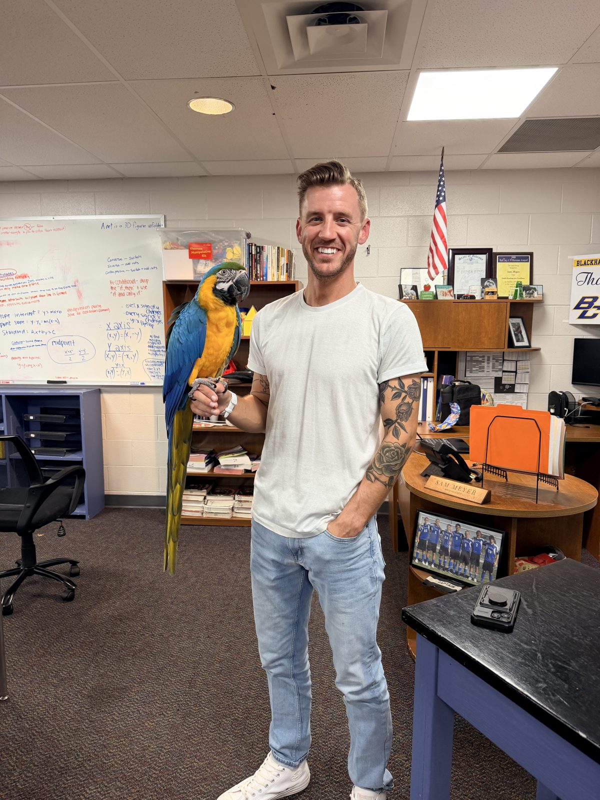 A smiling teacher holding a blue-and-gold macaw on his hand in a classroom